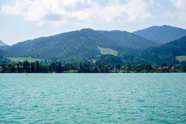 Bavyera Tegernsee Gölü 'nün manzarası ve arka planda dağlar olan kıyıları.                 