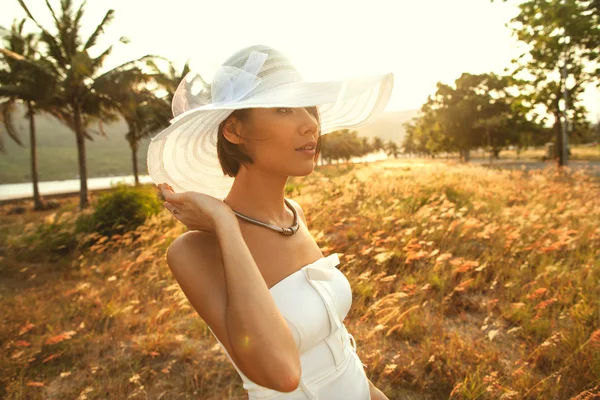 Hermosa chica de moda en sombrero y vestido blanco con un ramo de — Foto de Stock