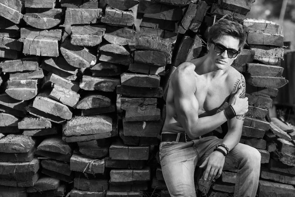 Elegantní muž v sluneční brýle sedí poblíž dřevěné pozadí, móda dív — Stock fotografie