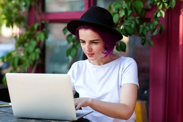紫色の髪のフリーランサーの女の子がカフェに座ってコンピュータで仕事をしています — ストック写真