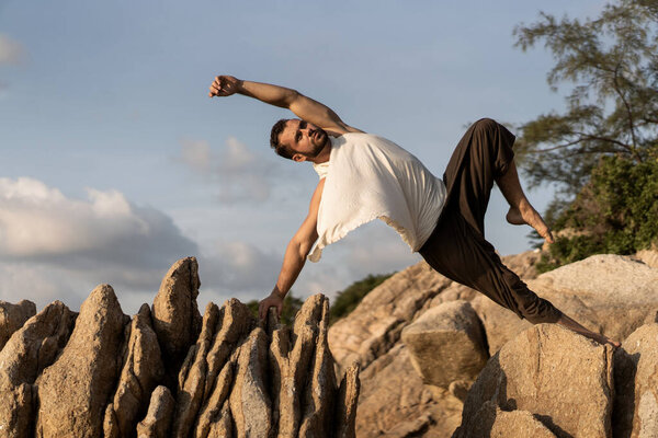 парень делает позы йоги на острых камнях рядом с пляжем в Таиланде