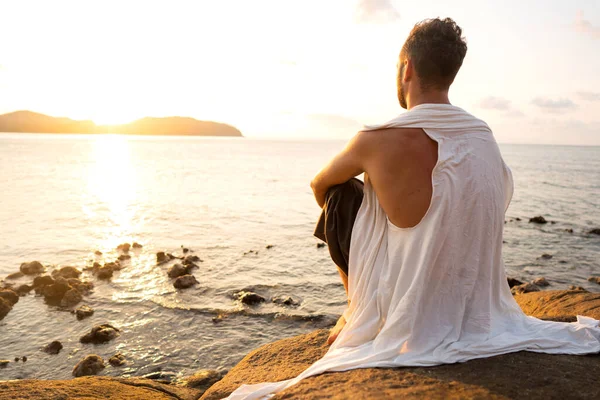 fashion guy on the beach at sunset makes meditation