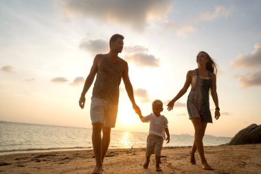 Mutlu aile gün batımında sahilde yürüyor.