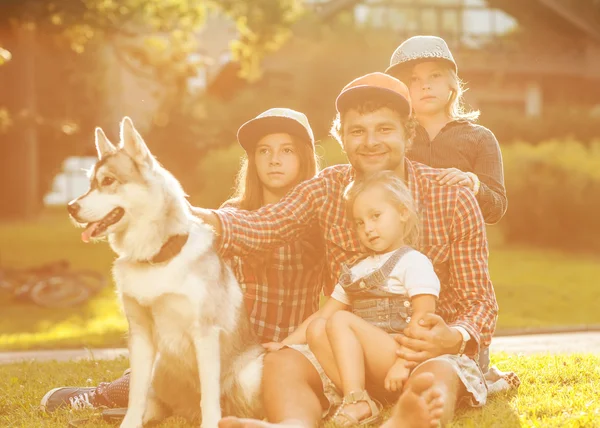 Vader en zijn 3 dochters en hond liggen op het gras in zonnebril gelukkig. — Stockfoto