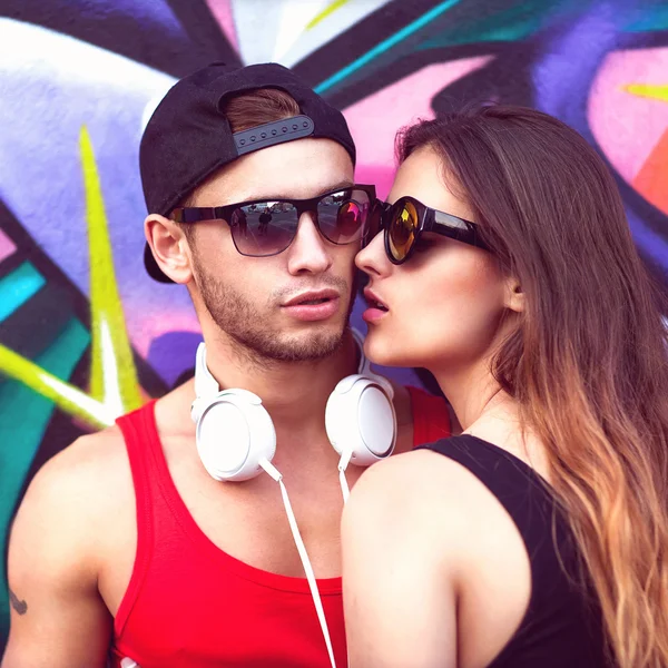 Fashion couple with sunglasses near the wall graffiti — Stock Photo, Image