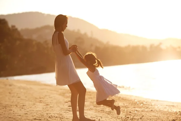 Mãe e filha na praia ao pôr do sol feliz — Fotografia de Stock
