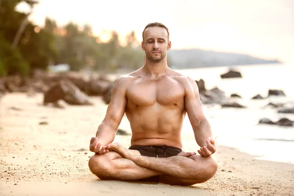 Muž cvičím jógu na pláži při západu slunce — Stock fotografie