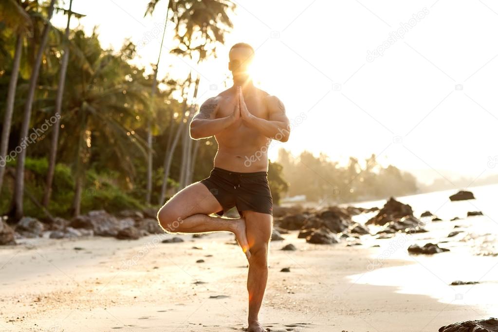 man practice yoga on the beach at sunset