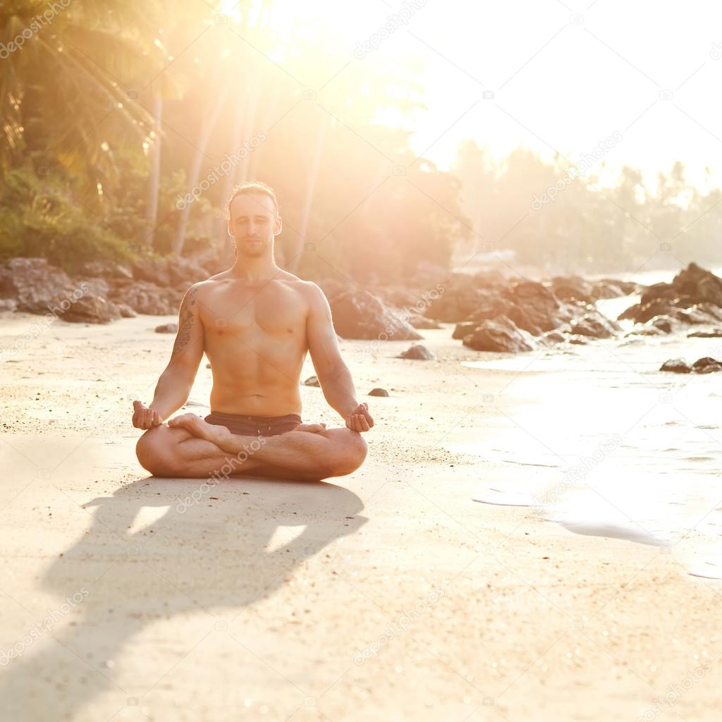 Man practice yoga on the beach at sunset