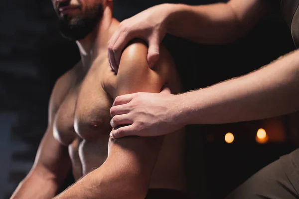Mężczyzna ramię i mięsień naramienny masaż do sportowca muskularny mężczyzna w ciemnym pokoju salon spa podczas siedzenia — Zdjęcie stockowe