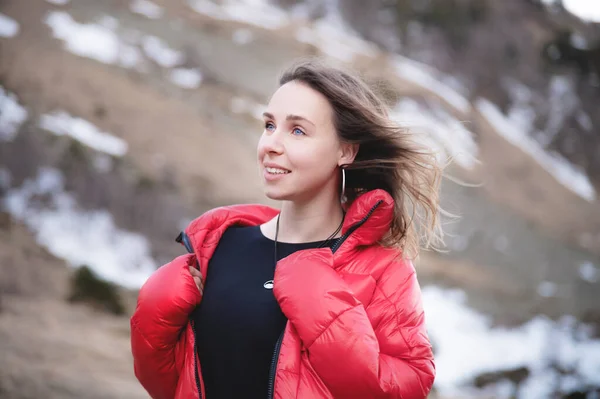 Retrato de uma jovem loira com olhos azuis brilhantes em um vestido preto e uma jaqueta vermelha para baixo caminha na queda nas montanhas. Caminhe nas terras altas — Fotografia de Stock