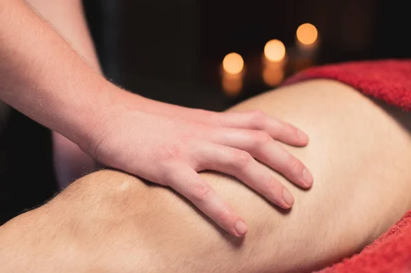 Massagista masculino fazendo massagem esportiva do joelho a um homem atleta em um quarto escuro de um salão de spa — Fotografia de Stock