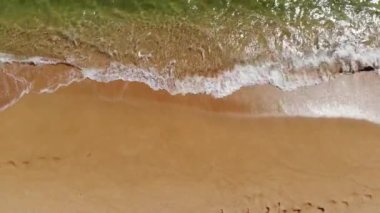 Deniz dalgaları üzerinde, kumlu sahilde yuvarlanan hava manzaralı alçak uçuş. Deniz kabuğu kumsalının arkasında sakin bir sörf