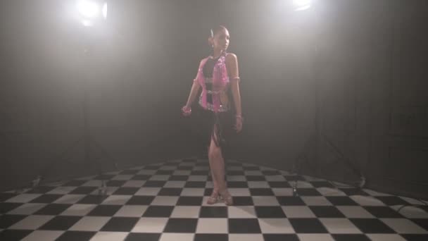 Atraktivní dospívající dívka v krásné růžové černé šaty profesionálně tančí taneční sál sportovní tanec sambu latino americké tance v tmavé místnosti naplněné kouřem — Stock video