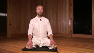 Uzun saçlı adam qigong ve yoga uygulayıcısı lotus pozisyonunda oturup meditasyon salonunun karanlık odasında pratik yapmaktan bahsediyorlar.