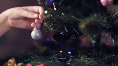 Manikürlü küçük bir kızın elinin sığ derinliği yapay bir Noel ağacına güzel oyuncaklar asıyor.