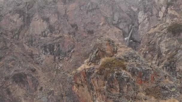 Volando más allá de las rocas altas en las montañas durante una nevada vista aérea de la cascada — Vídeo de stock