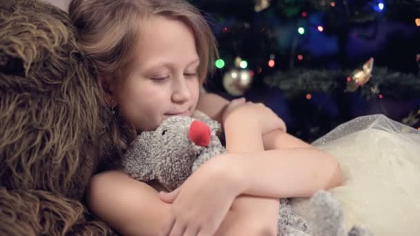 Año de la rata. Feliz niña caucásica cerca del árbol de Navidad abrazando a una rata de juguete. contra el fondo de luces intermitentes del árbol de Navidad — Vídeo de stock