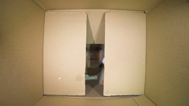 Egy hét éves kislány egy doboz repedésén keresztül kukucskál. Kilátás a dobozból. Ajándékmegelőzés és várakozás — Stock videók