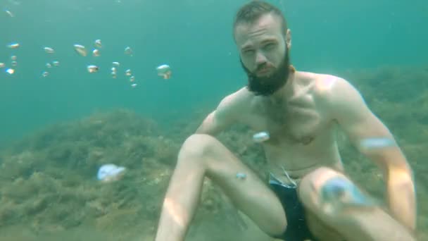 Un barbudo sin equipo submarino finge meditar en el mar. Movimiento lento — Vídeos de Stock