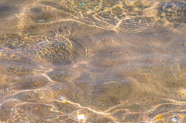 Suyun altındaki kumun bozulmuş dokusu. Şeffaf su dalgaları, kum dalgaları ve güneş ışığı. Deniz yatağı arkaplanı