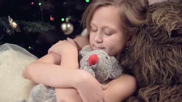 Año de la rata. Feliz niña caucásica cerca del árbol de Navidad abrazando a una rata de juguete. contra el fondo de luces intermitentes del árbol de Navidad — Vídeos de Stock