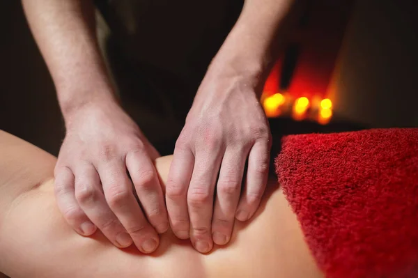 Close-up man handen van een masseur doet een dij massage naar een vrouw klant in een donkere kamer van een spa salon op een achtergrond van kaarsen — Stockfoto