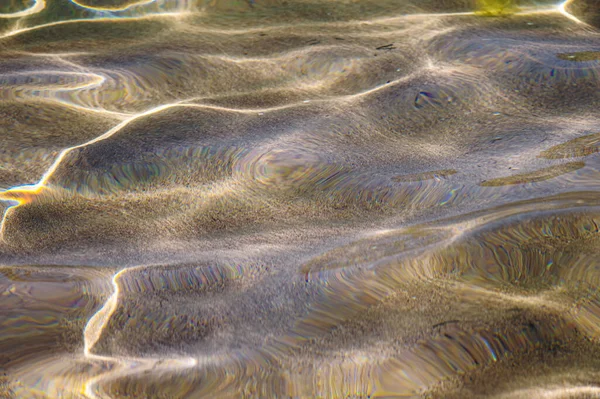 Close-up Textura distorsionada de arena bajo el agua. Ondas de agua transparentes, olas de arena y resplandor de la luz solar. Fondo del fondo marino —  Fotos de Stock