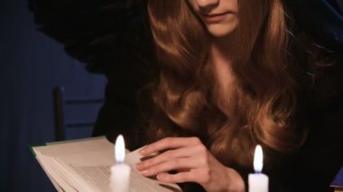 Uzun sarı saçlı, cadı kostümü giymiş, karanlık bir odada mum ışığında kalın bir kitap sayfasını karıştıran genç bir kadın. Cadılar Bayramı