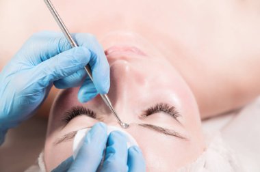 Mekanik yüz güzellik uzmanını soyar. Güzellik uzmanı, hastanın alnına tıbbi bir iğneyle sivilce sıkıyor. Kozmolojistin mavi eldivenlerinin yanında yüz. Yakın plan.