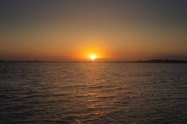 Sakin bir su yüzeyi olan bir körfez ya da göl üzerinde renkli bir günbatımı. Akşama doğru. Alçak tuş