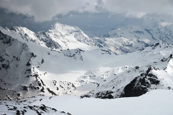 Rotsachtige hellingen met een gletsjer bedekt met sneeuw in de avond met lage bewolking — Stockfoto