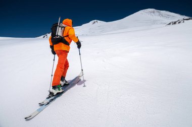 Sırt çantası, buz baltası, kayak ve direkleri olan bir dağcı Elbrus Dağı 'na bir kayak turuna çıkıyor. Taşra ve serbest kayak konsepti