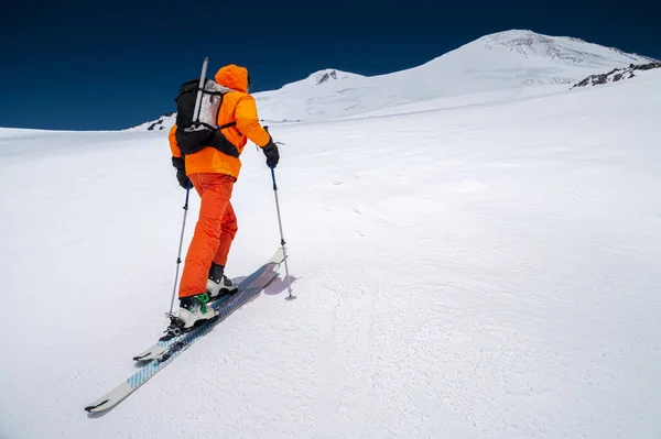 Ein Bergsteiger mit Rucksack, Eispickel, Skiern und Stöcken steigt auf eine Skitour zum Elbrus. Backcountry und Freeride-Konzept — Stockfoto