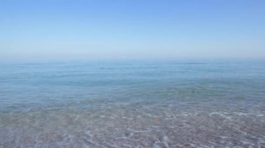 Sabahları mavi tonlarda ıssız bir sahil, kumlu sahilde küçük dalgalar akıyor. Denizin üstünde sis