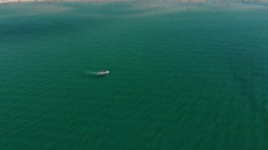 Güneşli bir günde turkuaz açık denizde yüzen bir motorlu teknenin hava görüntüsü. Deniz turizmi ve tekne gezileri.