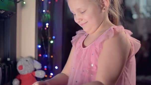 Little lonely cheerful fat girl playing with a soft toy rat on the background of an electric fireplace and blinking new year lights on christmas evening — Stock Video