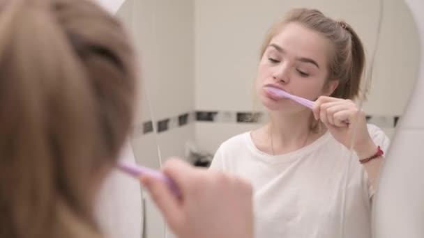 Jovem caucasiana sonolenta mulher escovando os dentes no banheiro pelo espelho — Vídeo de Stock