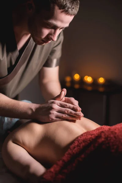 Massagista masculino fazendo massagem nas costas para a mulher cliente no quarto escuro do spa de massagem — Fotografia de Stock