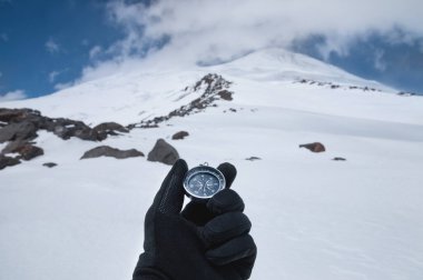 Siyah eldivenli bir adam, kar kaplı bir yamacın ve Elbrus Dağı 'nın iki zirvesinin arkasında manyetik bir pusula tutuyor. Kuzey Kafkasya 'da Turizm