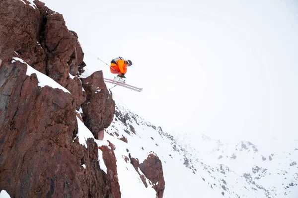 Mannelijke skiër atleet doet een drop sprong van een klif in de besneeuwde bergen op een bewolkte dag in de winter — Stockfoto