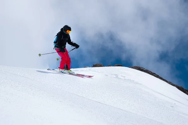 Vrouwelijke skiër maakt een sprong in de vlucht op een besneeuwde helling tegen de achtergrond van een blauwe hemel van bergen en wolken. Freeride en extreem skiën voor vrouwen — Stockfoto