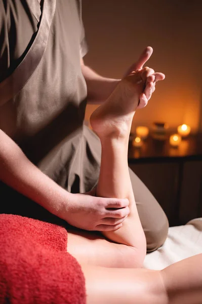 Profesionální masáž ženských nohou masérem v tmavém lázeňském salonu se svíčkami — Stock fotografie
