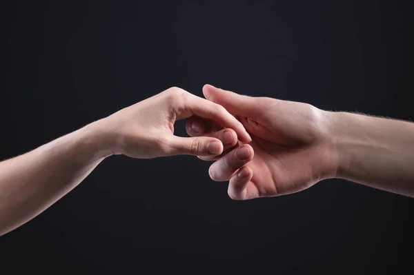 Twee handen houden elkaar vast. Symbool van tederheid, zorg en ondersteuning door een man van een vrouw op een donkere achtergrond — Stockfoto