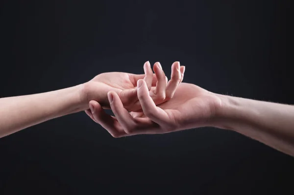 Две руки держатся друг за друга. Символ нежности, заботы и поддержки мужчины женщины на тёмном фоне — стоковое фото