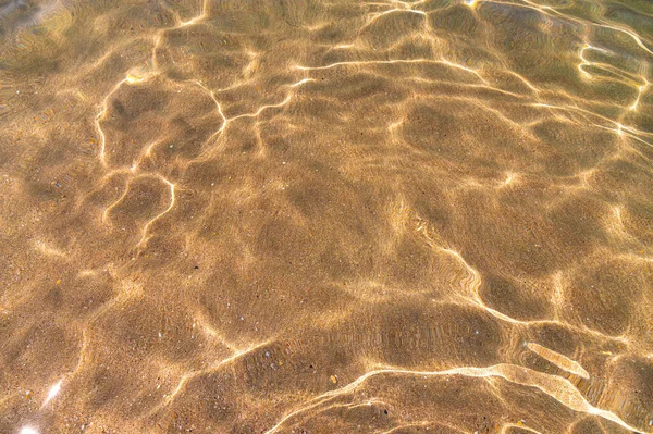 Textura distorsionada de arena bajo el agua. Ondas de agua transparentes, olas de arena y resplandor de la luz solar. Fondo del fondo marino —  Fotos de Stock