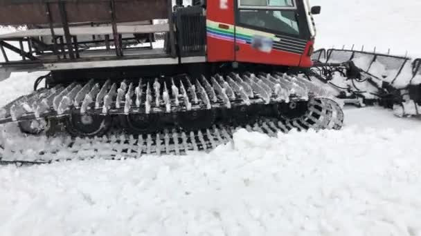 Close-up work of wide snowcat rides on snow and rakes it against the backdrop of snow-capped mountains. concept of preparing snow slopes for the ski season and snow harvesting — Stock Video