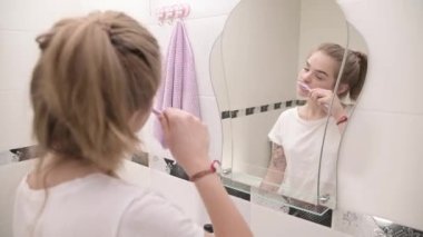 Genç, uykulu, uykulu kadın aynanın yanında dişlerini fırçalıyor.