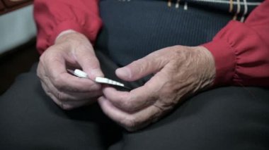 Yaşlı bir kadın, elinde tabletlerle odada bir sandalyeye oturan yaşlı bir kadın. Su toplayan tabletlerden alır