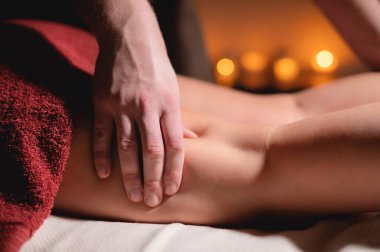 Erkek masör, spa salonunun karanlık bir odasında hasta bir kadına diz masajı yapıyor.